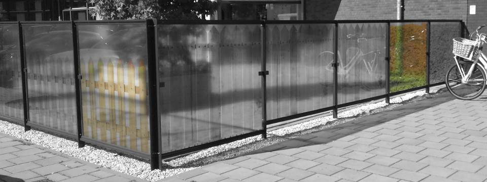Metalen hek met glazen panelen met daarop foto's van houten hekjes en een heg.